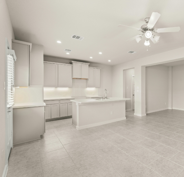 An expansive kitchen with tile floors, white cabinetry, and bright ceiling can lights, all in an empty setting.
