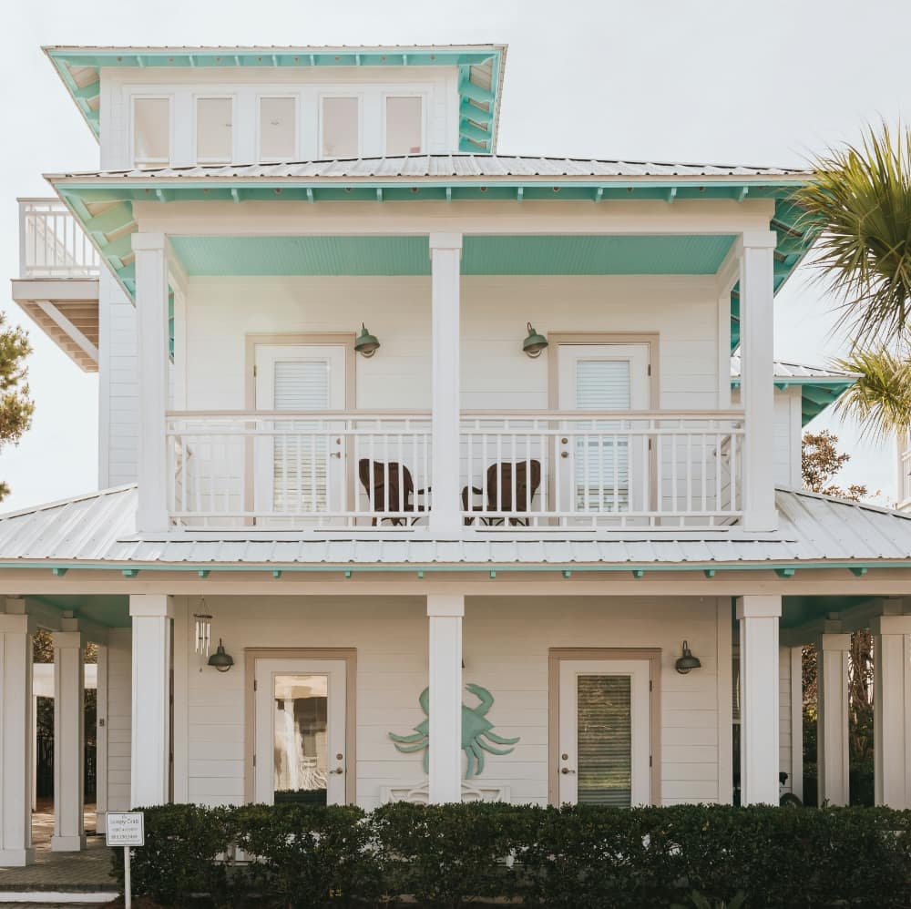 Remodeled coastal-style home with white siding, teal trim, and balcony